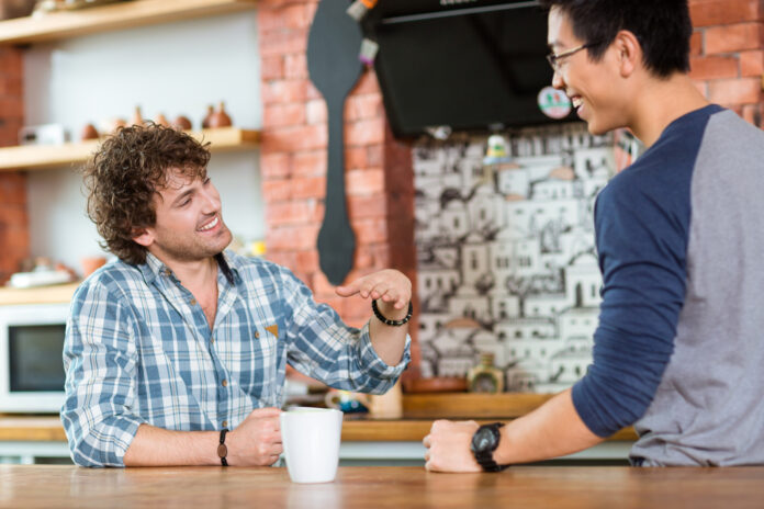 Two excited cheerful guys sitting, talking and laughing in cafe